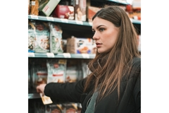 A woman grabs the price tag on at item on the shelf at the grocery store while looking unhappy.
